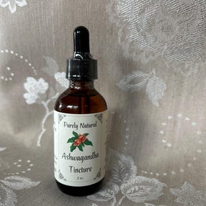 K&ouml;nnte beinhalten: Eine braune Glasflasche mit Tropfer. Das Etikett ist wei&szlig; mit schwarzem Text, der "Purely Natural Ashwagandha Tincture 2 oz." lautet. Auf dem Etikett befindet sich eine kleine Illustration einer roten Beere mit gr&uuml;nen Bl&auml;ttern.