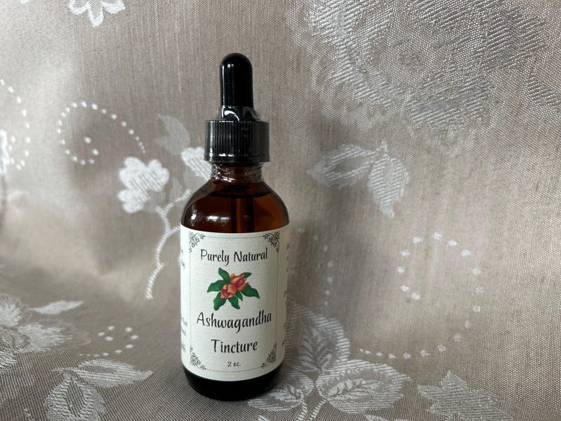 K&ouml;nnte beinhalten: Eine braune Glasflasche mit Tropfer. Das Etikett ist wei&szlig; mit schwarzem Text, der "Purely Natural Ashwagandha Tincture 2 oz." lautet. Auf dem Etikett befindet sich eine kleine Illustration einer roten Beere mit gr&uuml;nen Bl&auml;ttern.