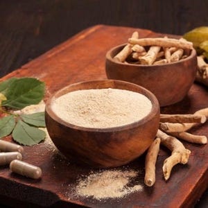 K&ouml;nnte beinhalten: Zwei Holzschalen, eine gef&uuml;llt mit hellem braunen Pulver und die andere mit getrockneten, hellbraunen Wurzeln. Die Schalen stehen auf einer Holzoberfl&auml;che mit ein paar Kapseln und einer gr&uuml;nen Pflanze.