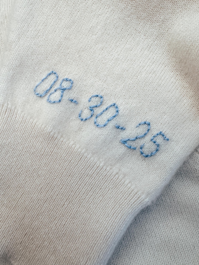 May include: White knitted fabric with blue embroidered text that reads "08.30.23".