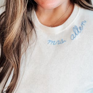 May include: A white sweater with blue embroidery that says "Mrs. Allen" on the front.