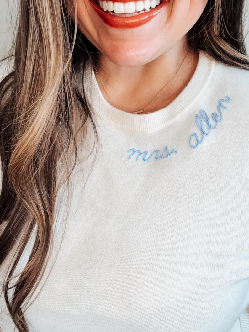 May include: A white sweater with blue embroidery that says "Mrs. Allen" on the front.