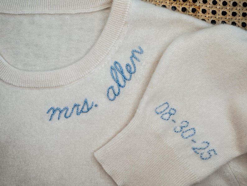 May include: A white knitted sweater with blue embroidery that reads "mrs. allen" and "08-30-23".