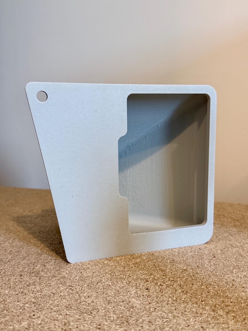 May include: A light gray, angular, open-faced container with a rectangular opening and a small hole in the upper left corner. The container has a smooth, matte finish and appears to be made of a solid material.
