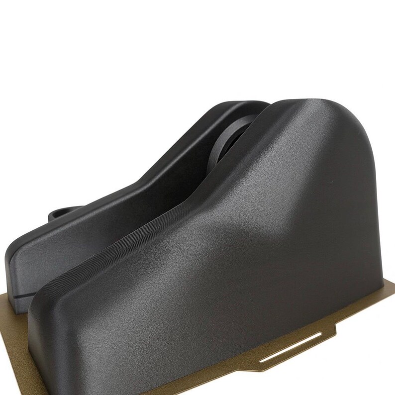 Puede incluir: Primer plano de dos componentes de pl&aacute;stico negro curvados, posiblemente parte de un ensamblaje m&aacute;s grande. Las piezas tienen un acabado liso y mate y est&aacute;n montadas sobre una base dorada. El dise&ntilde;o sugiere un producto funcional, posiblemente automotriz o industrial.