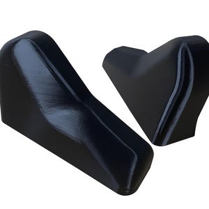 Puede incluir: Dos objetos negros angulares con un acabado liso y brillante. Uno tiene forma de cu&ntilde;a, el otro es m&aacute;s compacto y con forma de coraz&oacute;n. Los objetos parecen estar hechos de un material s&oacute;lido, posiblemente pl&aacute;stico o resina.