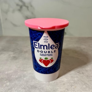 May include: A small pot of Elmlea Double cream with a pink lid. The container is dark blue with white text and a strawberry graphic. The text reads "Pour, Cook, Whip" and "A Deliciously Creamy Taste".