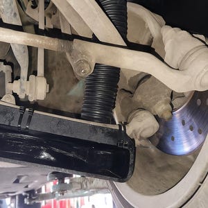 Puede incluir: Vista inferior del sistema de suspensi&oacute;n de un veh&iacute;culo, mostrando varios componentes. Se ven el amortiguador, el disco de freno y los brazos de control. La imagen destaca los detalles mec&aacute;nicos de los bajos del coche.