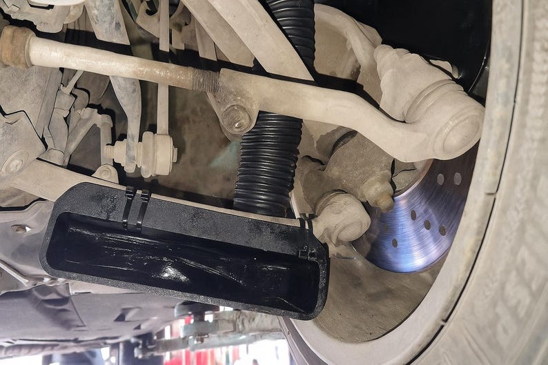 Puede incluir: Vista inferior del sistema de suspensi&oacute;n de un veh&iacute;culo, mostrando varios componentes. Se ven el amortiguador, el disco de freno y los brazos de control. La imagen destaca los detalles mec&aacute;nicos de los bajos del coche.