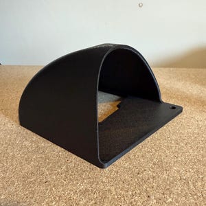 May include: A black, curved metal bracket with a flat base and a single mounting hole. The bracket has a rounded top and a rectangular opening, suitable for mounting or holding an item. The surface has a textured finish.