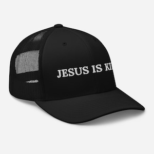 May include: Black trucker hat with a mesh back and a curved brim. The hat features the white text "JESUS IS KI" across the front. The hat is a classic style, suitable for casual wear.