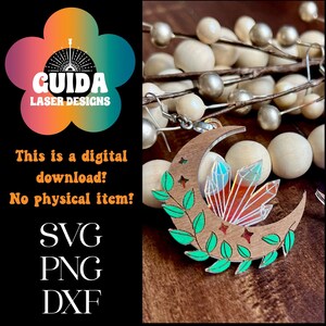 May include: A wooden crescent moon earring with a green leafy vine and a crystal design. The crystal is iridescent and has a red, orange, and blue color scheme. The earring is on a white background.