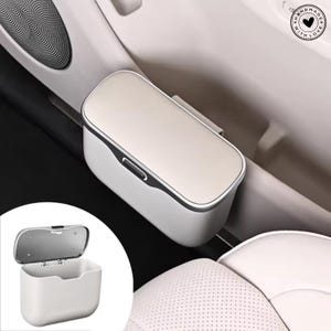 May include: A white and silver car trash bin with a hinged lid. The bin is rectangular with rounded edges and a silver trim. It is designed to attach to a car door or console.