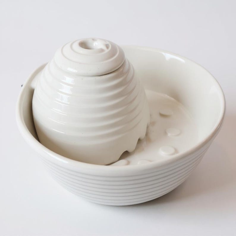 May include: A white ceramic citrus juicer set. The set includes a ridged, spiral-shaped reamer and a bowl with a spout and small raised circles. The bowl has horizontal ridges around the exterior.