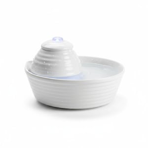 May include: A white ceramic pet water fountain with a tiered design. The fountain has a bowl-shaped base and a central, cone-shaped feature with a small, glowing light on top. Water is visible in the bowl.