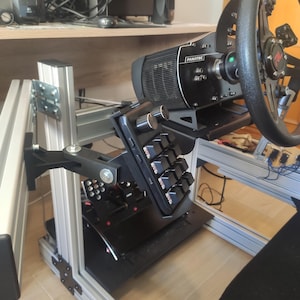 Può includere: Una base per volante da corsa Fanatec nera e un volante montati su un telaio in profilo di alluminio argentato. Un tastierino macro nero con due manopole argentate è fissato al telaio tramite un braccio regolabile, accanto ai pedali.