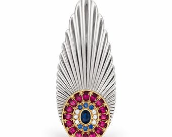 May include: A silver-toned brooch featuring a fan-shaped top and a circular base. The base is set with a central oval blue gemstone, surrounded by a ring of white stones, a ring of blue stones, and an outer border of oval red gemstones.