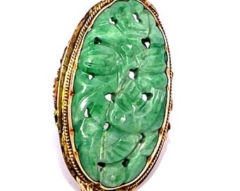 May include: Oval jade ring with a carved leaf design. The jade is a vibrant green color, set in a gold-toned filigree setting. The ring has an ornate, vintage appearance.