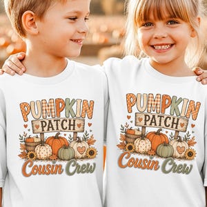 May include: Two white t-shirts featuring a graphic print with the text PUMPKIN PATCH COUSIN CREW. The design includes illustrations of various pumpkins, sunflowers, and autumn leaves in orange, green, and brown tones on the front of each shirt.