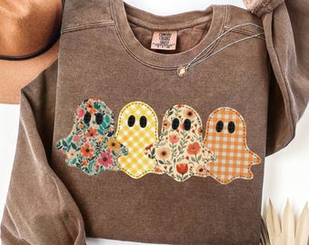 May include: A brown crewneck sweatshirt featuring a graphic of four ghosts in a row. The ghosts have different patterns: one with colorful flowers, one with yellow gingham, one with floral prints, and one with orange gingham. The label reads Comfort Colors.