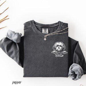 Puede incluir: Camiseta de manga larga gris oscuro con un gr&aacute;fico blanco de un perro Shih Tzu y el nombre "Bella". Un collar plateado con un colgante est&aacute; sobre la camisa. La palabra "pepper" est&aacute; impresa en la esquina inferior izquierda.