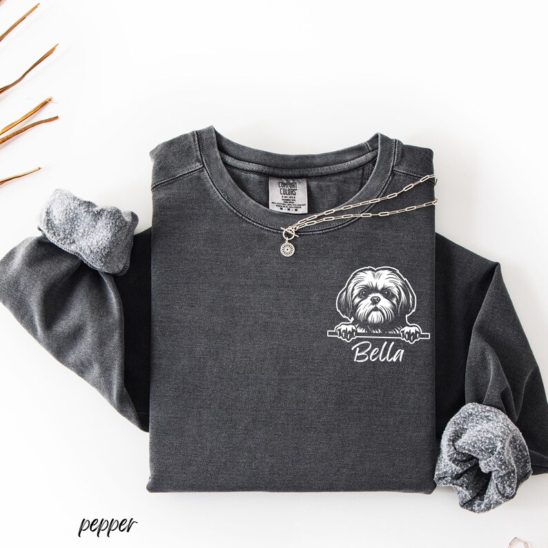 Puede incluir: Camiseta de manga larga gris oscuro con un gr&aacute;fico blanco de un perro Shih Tzu y el nombre "Bella". Un collar plateado con un colgante est&aacute; sobre la camisa. La palabra "pepper" est&aacute; impresa en la esquina inferior izquierda.