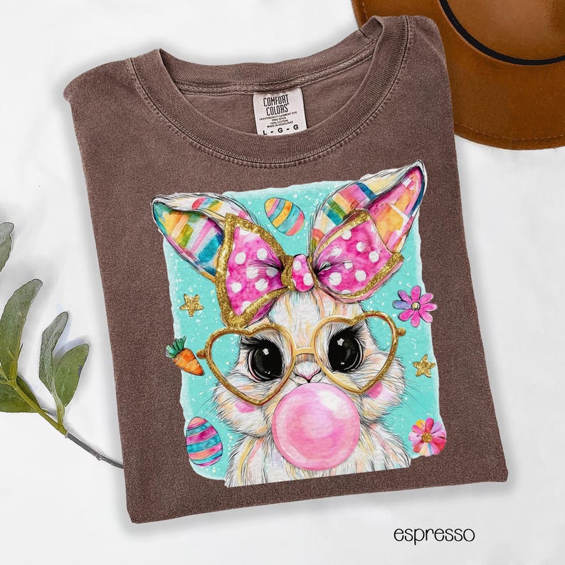 Peut inclure: T-shirt couleur expresso avec un lapin de dessin anim&eacute; portant des lunettes en forme de c&oelig;ur et soufflant une bulle de chewing-gum. Le lapin a un n&oelig;ud rose &agrave; pois blancs et des oreilles color&eacute;es. Le t-shirt porte l'&eacute;tiquette de la marque Comfort Colors.