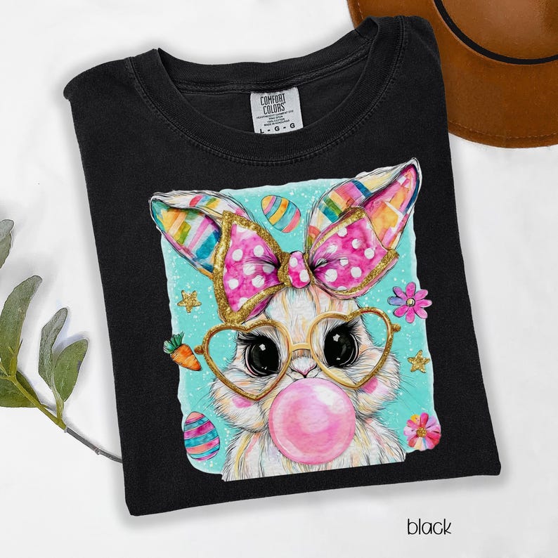 Peut inclure: T-shirt noir avec un motif de lapin de P&acirc;ques. Le lapin porte des lunettes en forme de c&oelig;ur et un n&oelig;ud rose, soufflant une bulle de chewing-gum. Le motif comprend des &oelig;ufs de P&acirc;ques et des fleurs. Le mot "black" est en bas.