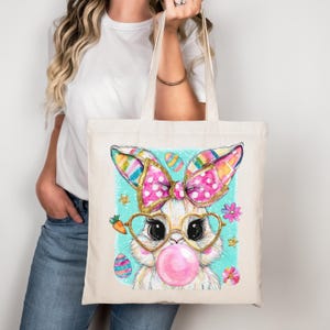 Peut inclure: Un sac fourre-tout cr&egrave;me avec un motif de lapin de P&acirc;ques fantaisiste. Le lapin porte des lunettes en forme de c&oelig;ur, une bulle rose et un n&oelig;ud &agrave; pois avec des paillettes dor&eacute;es. Des &oelig;ufs de P&acirc;ques et des fleurs entourent le lapin. Les oreilles sont ray&eacute;es.
