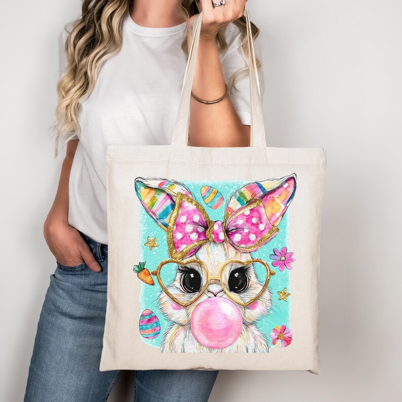 Peut inclure: Un sac fourre-tout cr&egrave;me avec un motif de lapin de P&acirc;ques fantaisiste. Le lapin porte des lunettes en forme de c&oelig;ur, une bulle rose et un n&oelig;ud &agrave; pois avec des paillettes dor&eacute;es. Des &oelig;ufs de P&acirc;ques et des fleurs entourent le lapin. Les oreilles sont ray&eacute;es.