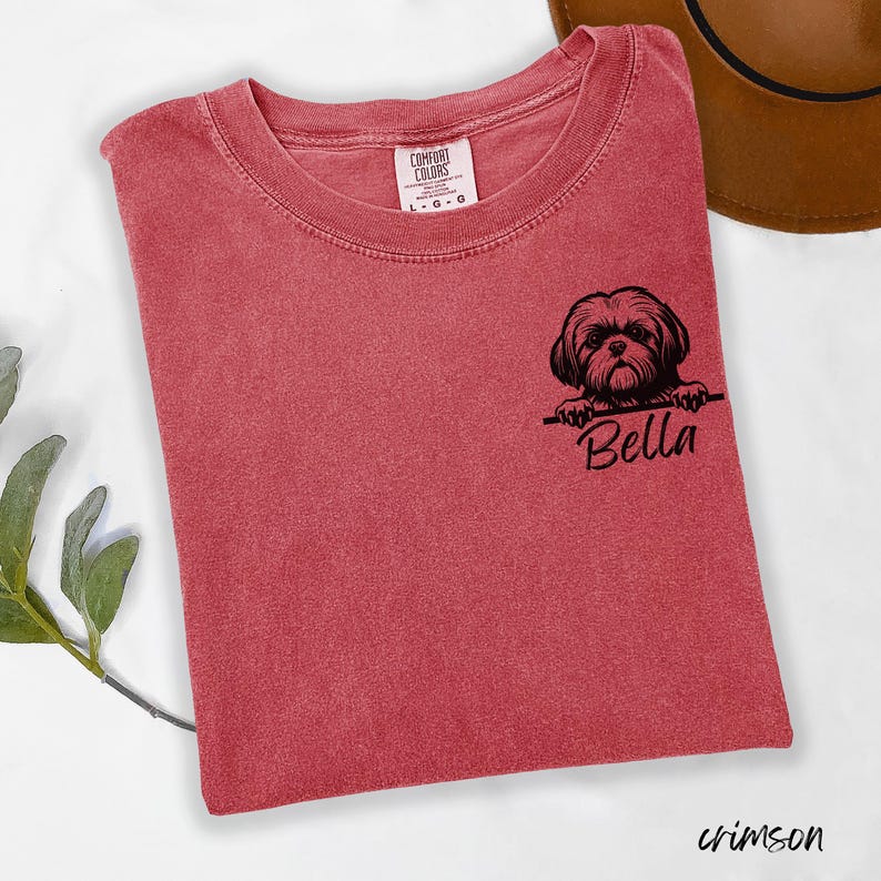 Puede incluir: Camiseta de color carmes&iacute; con cuello redondo. La camiseta presenta un gr&aacute;fico negro de un perro Shih Tzu con el nombre "Bella" debajo. La camiseta est&aacute; hecha por Comfort Colors.