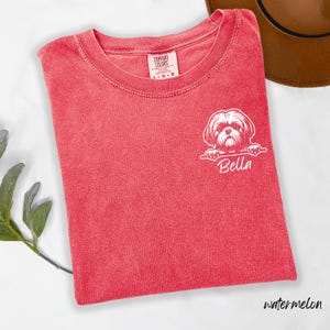 Puede incluir: Camiseta roja Comfort Colors con un gr&aacute;fico blanco de un perro Shih Tzu y el nombre "Bella" impreso debajo. La camiseta, talla L-G, est&aacute; doblada sobre una superficie blanca y etiquetada como "watermelon".