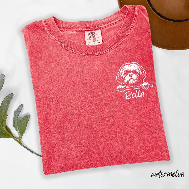 Puede incluir: Camiseta roja Comfort Colors con un gr&aacute;fico blanco de un perro Shih Tzu y el nombre "Bella" impreso debajo. La camiseta, talla L-G, est&aacute; doblada sobre una superficie blanca y etiquetada como "watermelon".