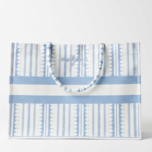 Könnte beinhalten: Eine rechteckige Tragetasche mit hellblauem und weißem Streifenmuster. Die Tasche hat vertikale Streifen mit einem gewellten Randdesign und horizontale Streifen. Das Wort "mahjong" ist auf die Tasche gedruckt. Die Griffe sind hellblau und weiß.