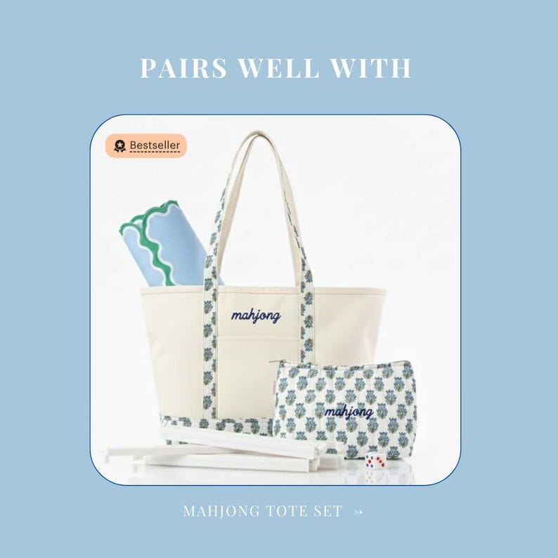 May include: A cream-colored canvas tote bag and a matching zippered pouch, both embroidered with the word mahjong in blue script. The set features a floral pattern on the straps and base, accompanied by a blue and green mat and white game sticks.