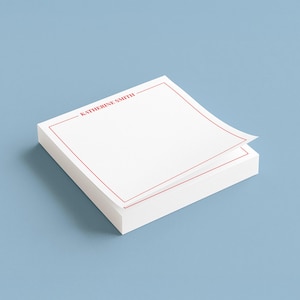 May include: A stack of white notepads with a red border and the name "KATHERINE SMITH" printed at the top. One sheet is slightly lifted, revealing the stack's edge. The background is a solid light blue.