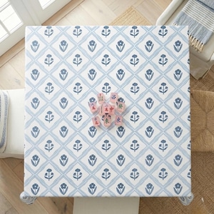 May include: Overhead view of a square table with a blue and white floral pattern. A set of pink Mahjong tiles are arranged on the table. The table is surrounded by a white bench, a chair, and a woven rug.