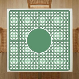 Puede incluir: Vista aérea de una mesa cuadrada blanca con un patrón tejido verde y blanco. El centro de la mesa tiene un círculo verde sólido. Sillas de mimbre son parcialmente visibles alrededor de la mesa.