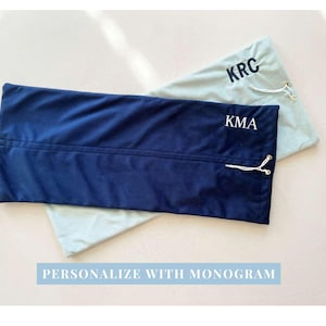 May include: Two rectangular fabric pouches with drawstring closures. One pouch is dark navy blue with the white embroidered monogram KMA, and the other is light sage green with the black embroidered monogram KRC. Text reads PERSONALIZE WITH MONOGRAM.