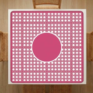 Pu&ograve; includere: Vista dall'alto di un tavolo quadrato con cornice bianca e motivo intrecciato rosa. Il centro presenta un cerchio rosa pieno. Sedie in vimini parzialmente visibili, che suggeriscono un ambiente da pranzo o all'aperto.