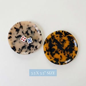 May include: Two round coasters with a tortoiseshell pattern. One coaster is beige with black spots, and the other is amber with black spots. Two dice with red and blue dots are on one coaster. The text "3.5 X 3.5" SIZE" is at the bottom.