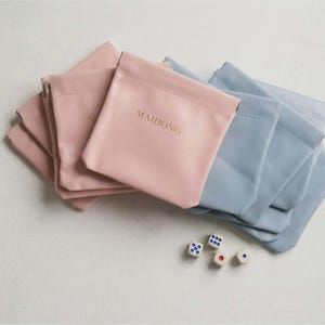 May include: A collection of pink and blue pouches with the word "MAHJONG" printed on one. Several dice with white and blue dots are scattered near the pouches. The pouches are made of a smooth material.
