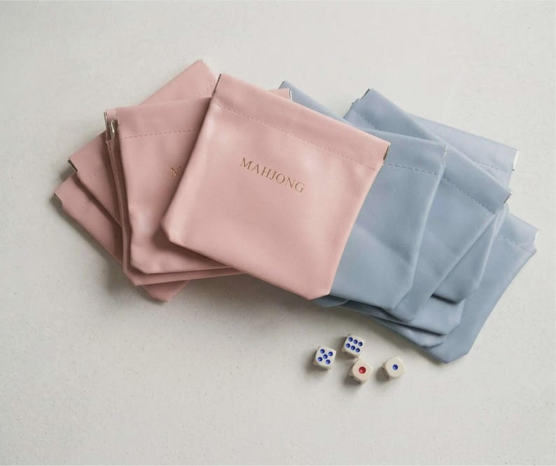 May include: A collection of pink and blue pouches with the word "MAHJONG" printed on one. Several dice with white and blue dots are scattered near the pouches. The pouches are made of a smooth material.