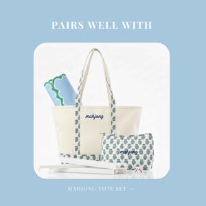 May include: A cream-colored Mahjong tote set with a matching pouch and a blue and green patterned trim. The tote bag and pouch have the word "mahjong" embroidered in blue. The set includes a blue mat and game accessories.