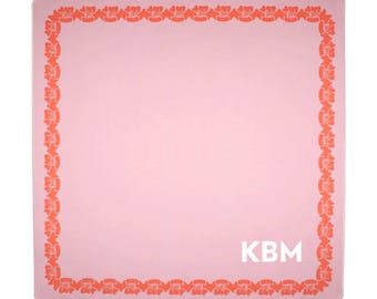 May include: A square, pink mousepad with a border of orange floral designs. The center of the mousepad has the white initials "KBM". The mousepad is a solid pink color.