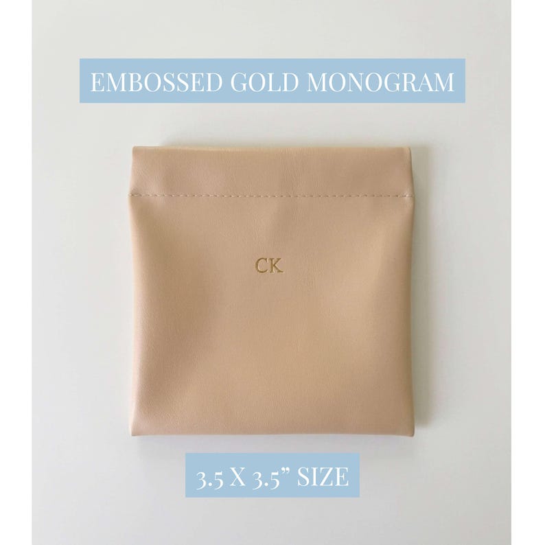 May include: A beige square pouch with the embossed gold monogram "CK". The text "EMBOSSED GOLD MONOGRAM" and "3.5 X 3.5" SIZE" are in light blue rectangles above and below the pouch. The pouch is 3.5 inches by 3.5 inches.