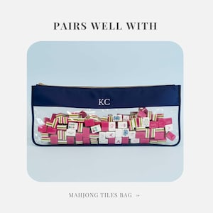 May include: A navy blue Mahjong tiles bag with a clear front, gold zip, and the initials "KC". The bag is filled with pink, white, and green Mahjong tiles. Text at the top reads "PAIRS WELL WITH" and at the bottom "MAHJONG TILES BAG".