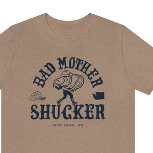 May include: A tan t-shirt with a navy blue graphic of a person carrying a large pile of oysters. The graphic is surrounded by the text "Bad Mother Shucker" and "Hood Canal, WA".