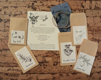 Pode incluir: Uma coleção de materiais de artesanato, incluindo pequenos pacotes de papel rotulados com "Cascas de ovo", "Alecrim", "Sal marinho", "Erva de São João" e "Raspa de limão". Uma nota manuscrita e um quadrado de tecido azul também estão incluídos.