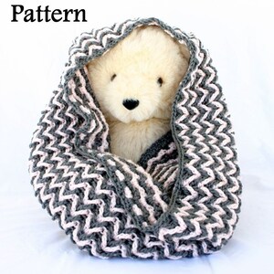 May include: A gray and pink chevron knit cowl, large enough to fit a stuffed animal. The cowl is made with a simple stitch pattern and is a great beginner project.